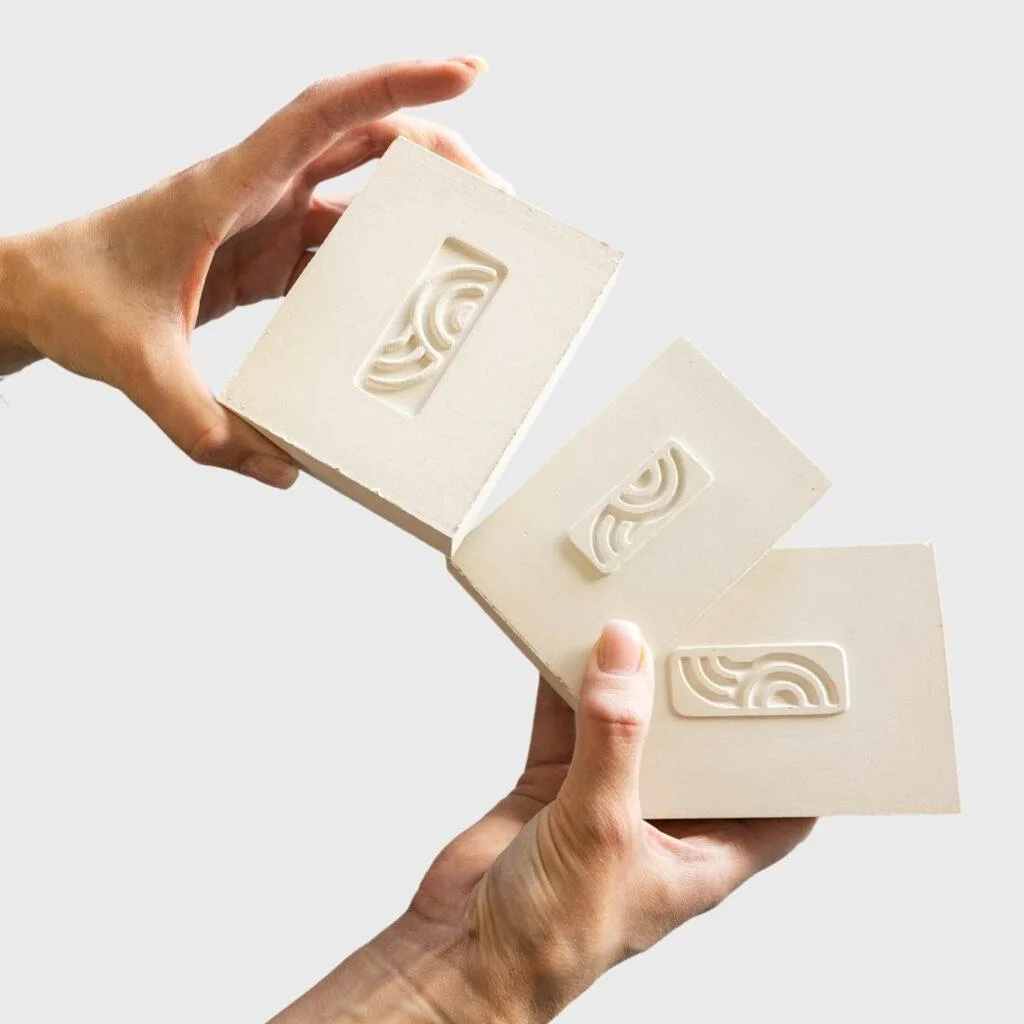 Three cream Fika tiles held in two hands, each with a raised arc pattern.